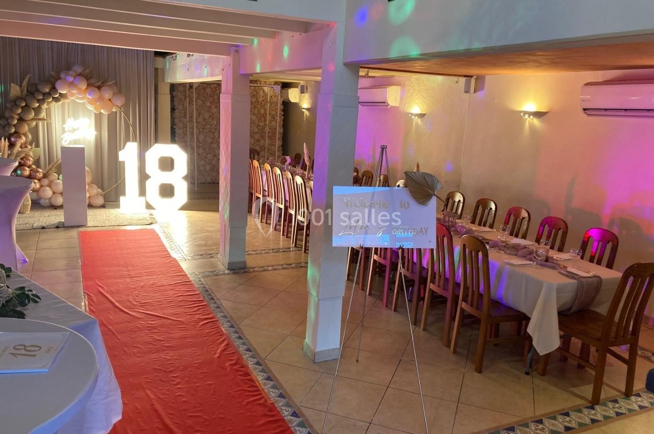 Salle décorée pour une fête d'anniversaire avec un tapis rouge, des tables dressées et un grand chiffre 18 lumineux.