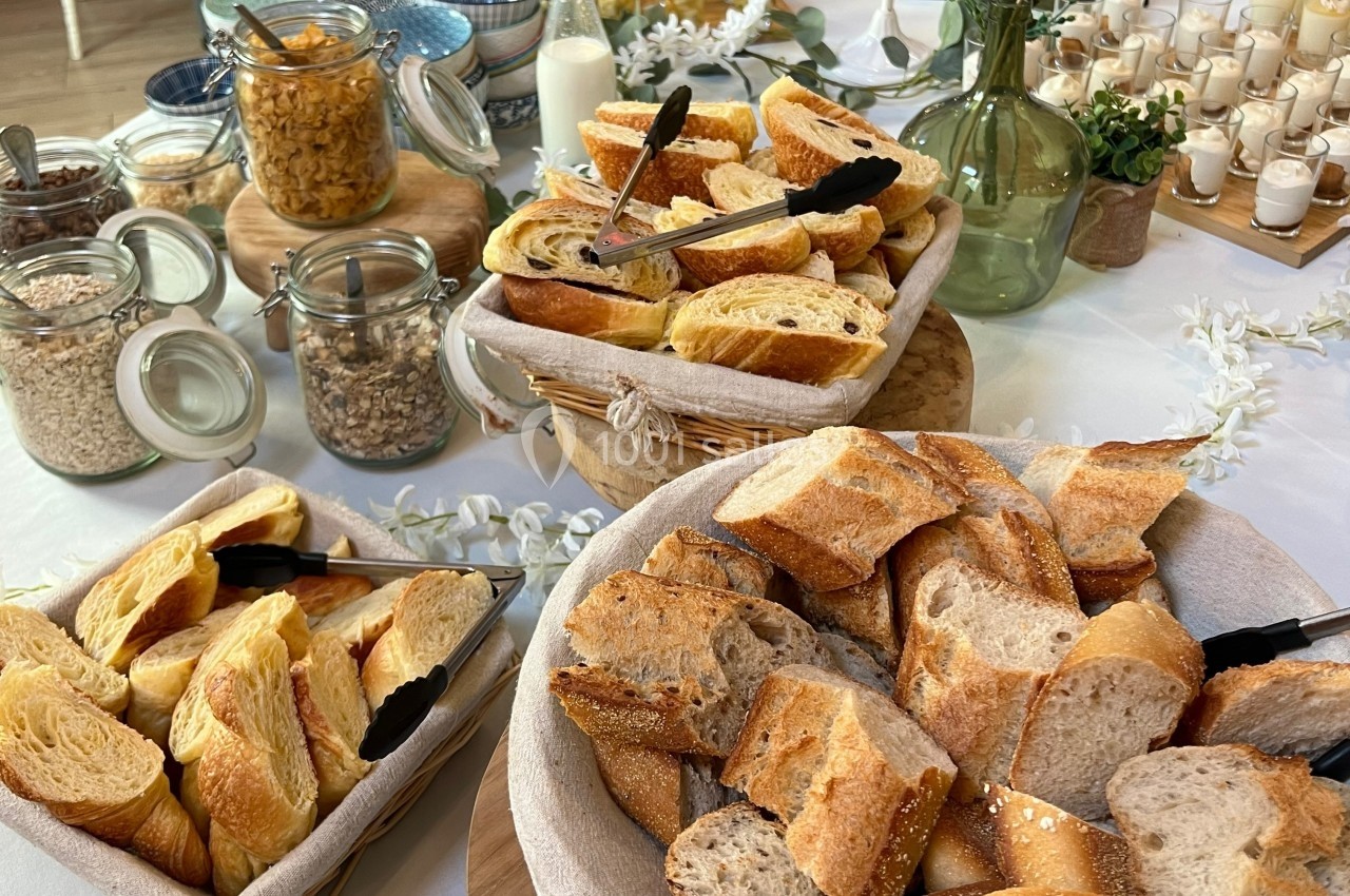 Assortiment de pains et viennoiseries disposés dans des paniers sur une table avec des céréales et des verrines en arrière…