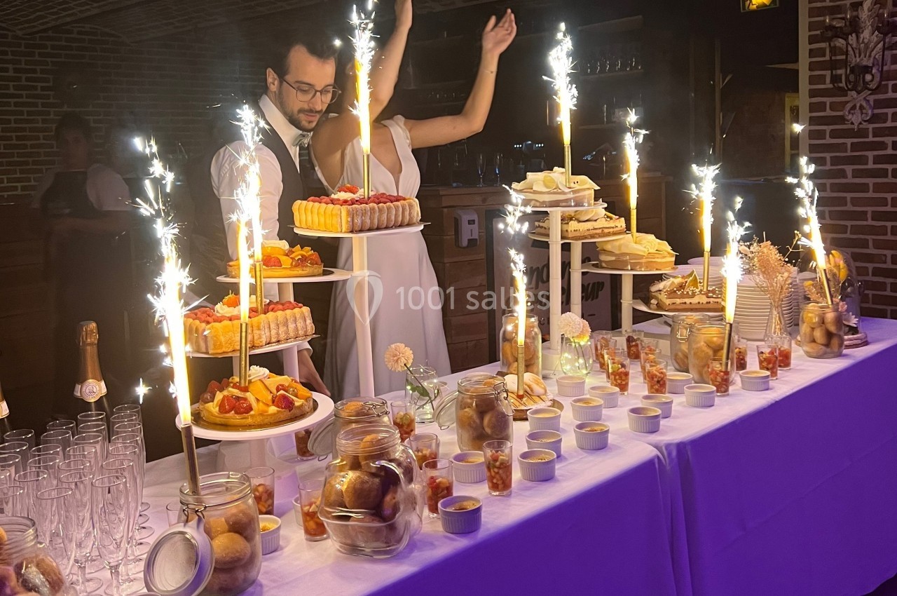 Table de desserts décorée avec des fontaines lumineuses, comprenant gâteaux, verrines et friandises dans un cadre festif.