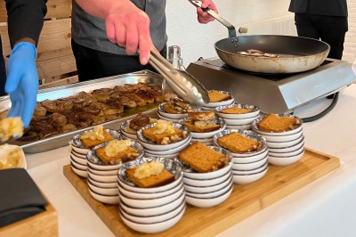 Plateau de mini-sandwiches variés, wraps et brochettes apéritives avec tomates cerises, présenté dans une boîte ouverte.