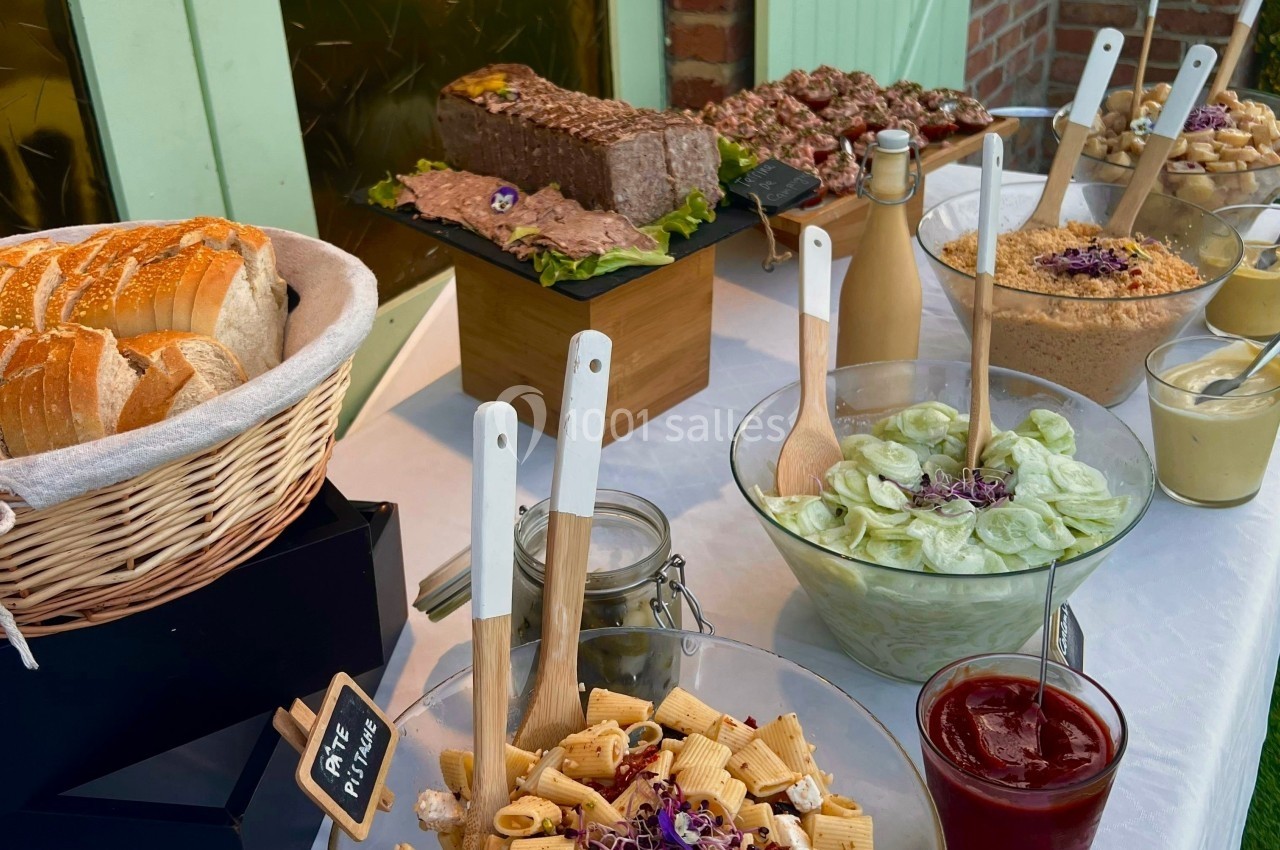 Buffet avec pain, pâté, salades variées, pâtes, condiments et sauces, présenté sur une table blanche.