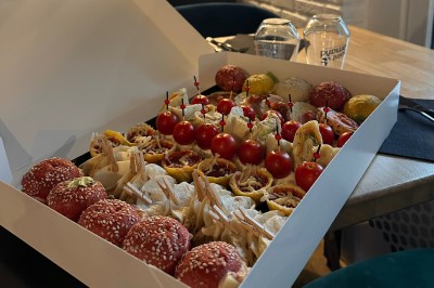 Plateau de mini-sandwiches variés, wraps et brochettes apéritives avec tomates cerises, présenté dans une boîte ouverte.