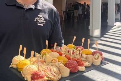 Plateau de mini-sandwiches variés, wraps et brochettes apéritives avec tomates cerises, présenté dans une boîte ouverte.