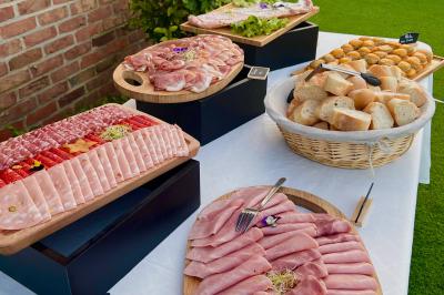 Plateau de charcuterie variée, pain et petits pains disposés sur une table blanche en extérieur.