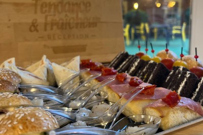 Plateau de mini-sandwiches variés, wraps et brochettes apéritives avec tomates cerises, présenté dans une boîte ouverte.