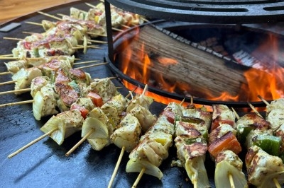 Miniature Traiteur Leers (Nord) - Tendance et Fraicheur Traiteur #16 Brochettes de viande et légumes grillant sur un barbecue en plein air, avec une fontaine et un jardin en arrière-plan.