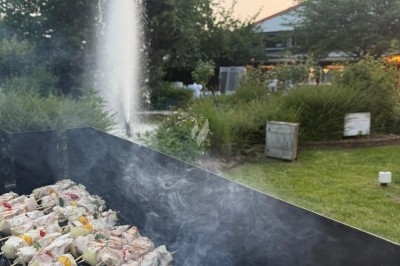 Miniature Traiteur Leers (Nord) - Tendance et Fraicheur Traiteur #19 Brochettes de viande et légumes grillant sur un barbecue en plein air, avec une fontaine et un jardin en arrière-plan.