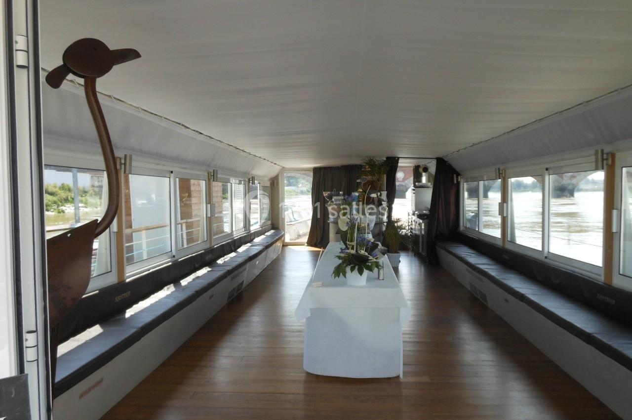 Intérieur d'une péniche aménagée avec des bancs, un sol en bois et une table décorée au centre.