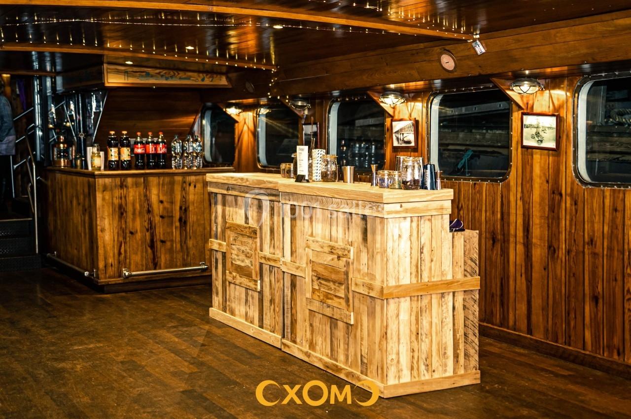 Bar en bois rustique dans un intérieur de bateau, avec des boissons et des verres disposés sur le comptoir.