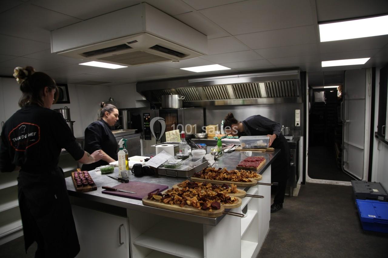 Trois cuisiniers préparent des plats dans une cuisine professionnelle équipée, avec des assiettes déjà dressées au premier…