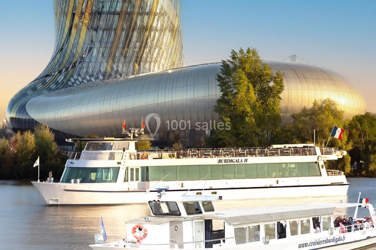 Deux bateaux de croisière naviguent sur une rivière devant un bâtiment moderne aux formes courbes.