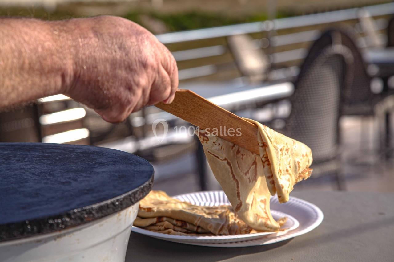 Une main dépose une crêpe chaude sur une assiette à l'aide d'une spatule en bois près d'une crêpière.