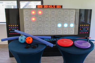 Miniature Multitudes de jeux sur le mur interactif Mur interactif lumineux avec chronomètre, accessoires de sport et équilibre disposés sur deux tables bleues au premier plan.