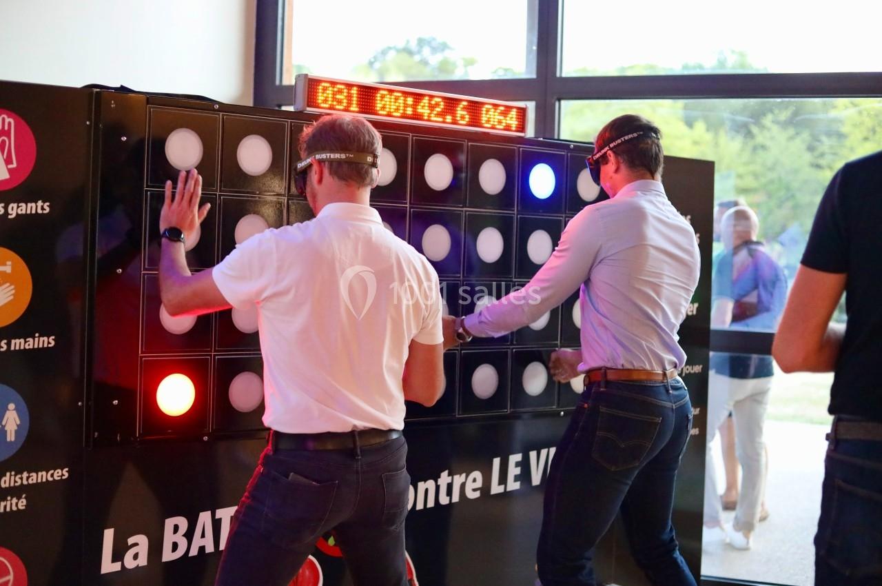 Deux hommes jouent à un jeu interactif lumineux sur un mur tactile dans un espace intérieur.