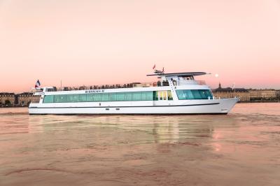 Bateau blanc naviguant sur une rivière au coucher du soleil, avec des bâtiments historiques en arrière-plan.