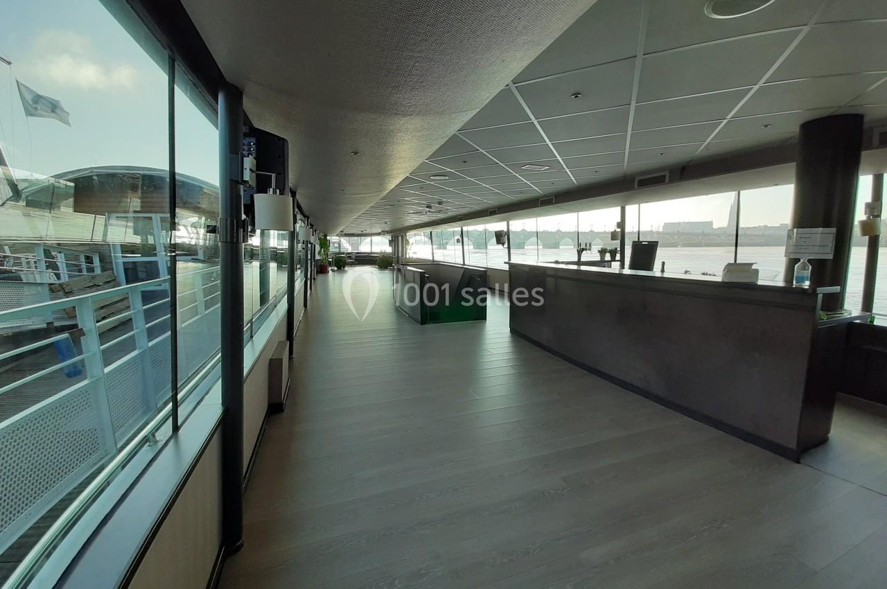 Intérieur lumineux d'un bateau avec un comptoir à droite, des fenêtres donnant sur l'eau et un pont extérieur visible.
