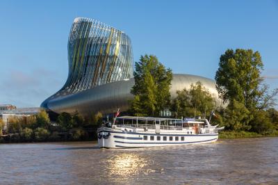 Bâtiment moderne en verre et métal près d'un fleuve, avec un bateau blanc amarré au premier plan.