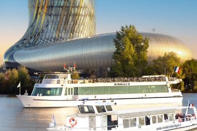 Bâtiment moderne en verre et métal près d'un fleuve, avec un bateau blanc amarré au premier plan.