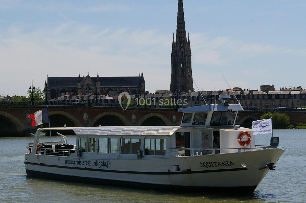Bateau de croisière fluvial naviguant sur une rivière, avec un pont et une église en arrière-plan.