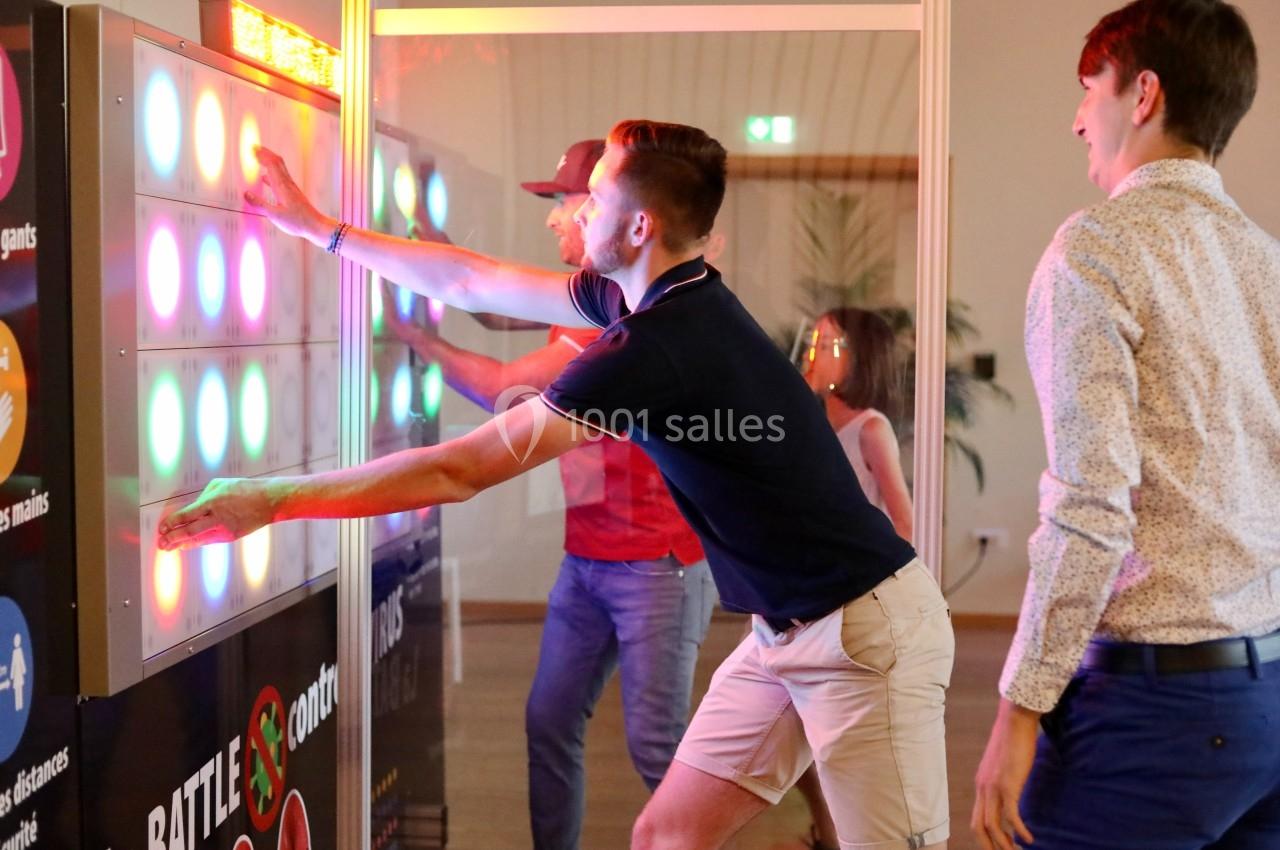 Des personnes jouent à un jeu interactif lumineux, appuyant sur des boutons colorés dans un cadre intérieur.