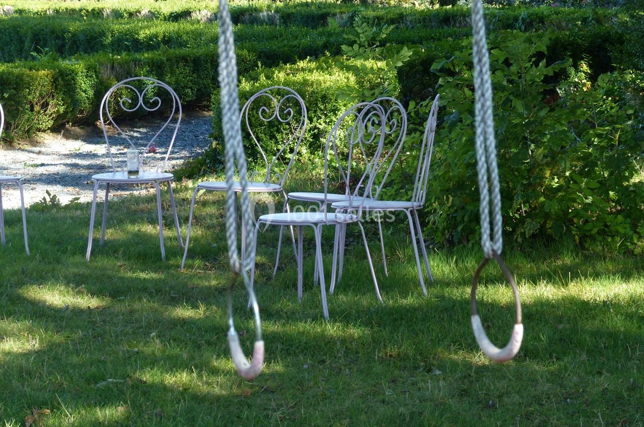 Chaises en métal blanc et table assortie disposées sur une pelouse, avec des anneaux de balançoire au premier plan.