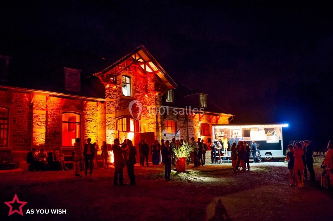 Bâtiment en pierre éclairé en rouge la nuit, avec des groupes de personnes et un food truck à proximité.