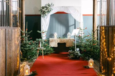 Un couple en tenue de mariage se tient devant un officiant dans un décor festif avec sapins et guirlandes lumineuses.