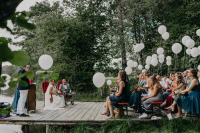 Un couple en tenue de mariage se tient devant un officiant dans un décor festif avec sapins et guirlandes lumineuses.
