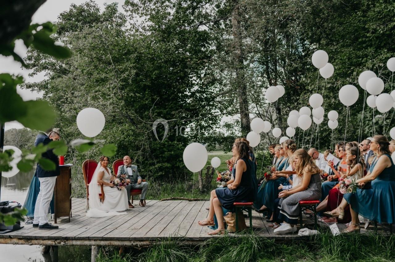 Cérémonie de mariage en plein air sur un ponton, avec des invités assis et des ballons blancs décoratifs.