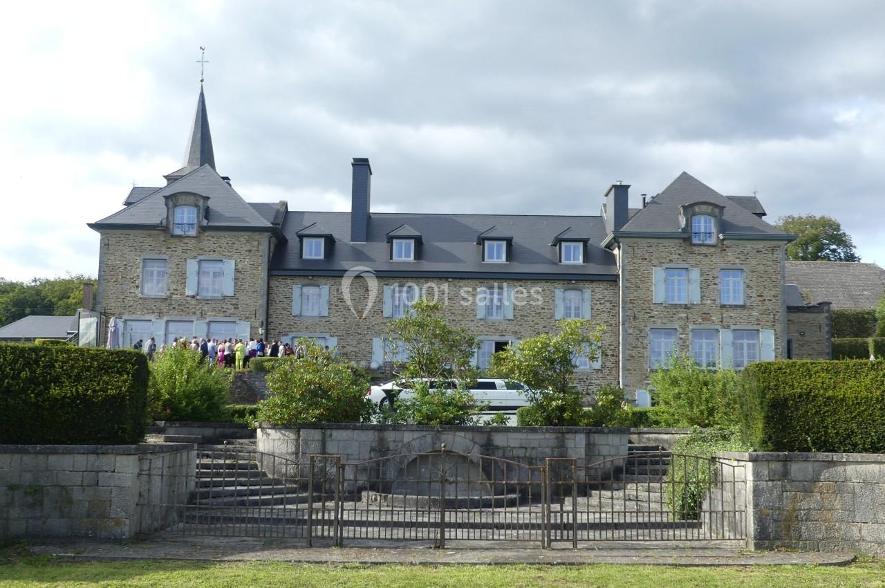 Façade d'un grand bâtiment en pierre avec un toit en ardoise, entouré de jardins et d'une grille métallique.