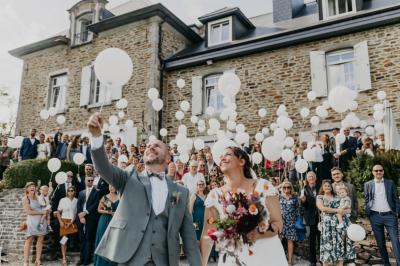 Un couple en tenue de mariage se tient devant un officiant dans un décor festif avec sapins et guirlandes lumineuses.