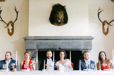 Un couple en tenue de mariage se tient devant un officiant dans un décor festif avec sapins et guirlandes lumineuses.