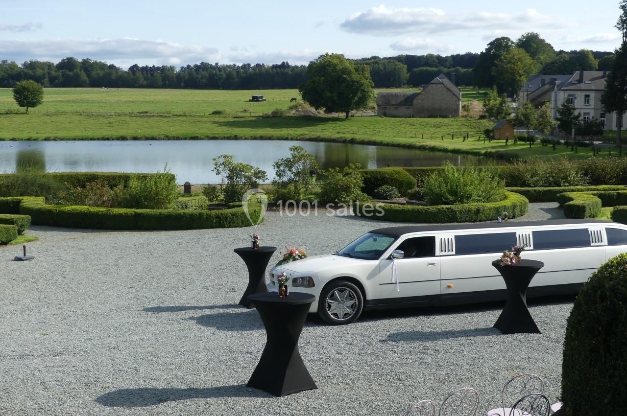 Limousine blanche garée sur une allée gravillonnée devant un jardin paysager avec un étang en arrière-plan.