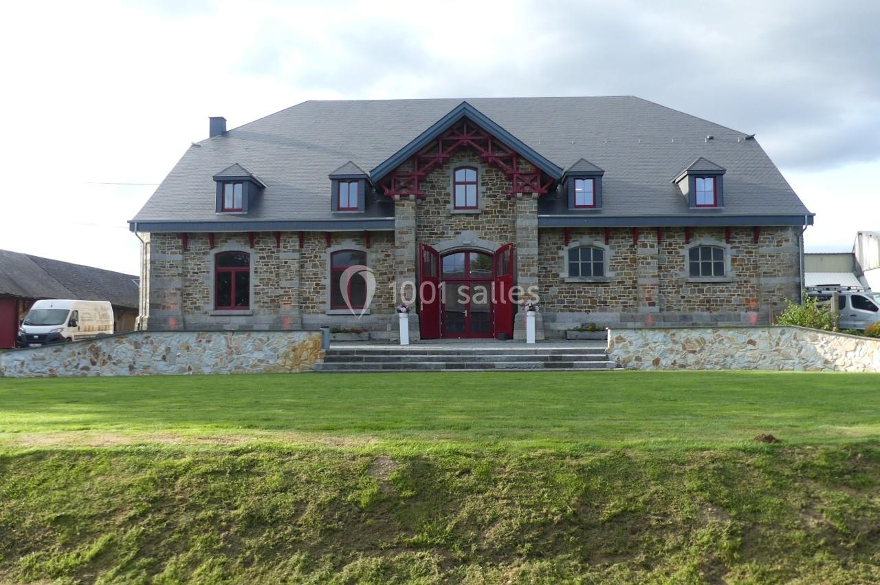 Façade d'une grande maison en pierre avec toit en ardoise, fenêtres mansardées et entrée centrale encadrée de rouge.