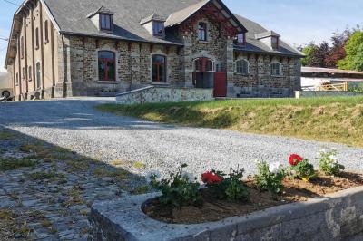 Porte d'entrée rouge à double battant ouverte, entourée d'un mur en pierre, avec des pots de fleurs de chaque côté.