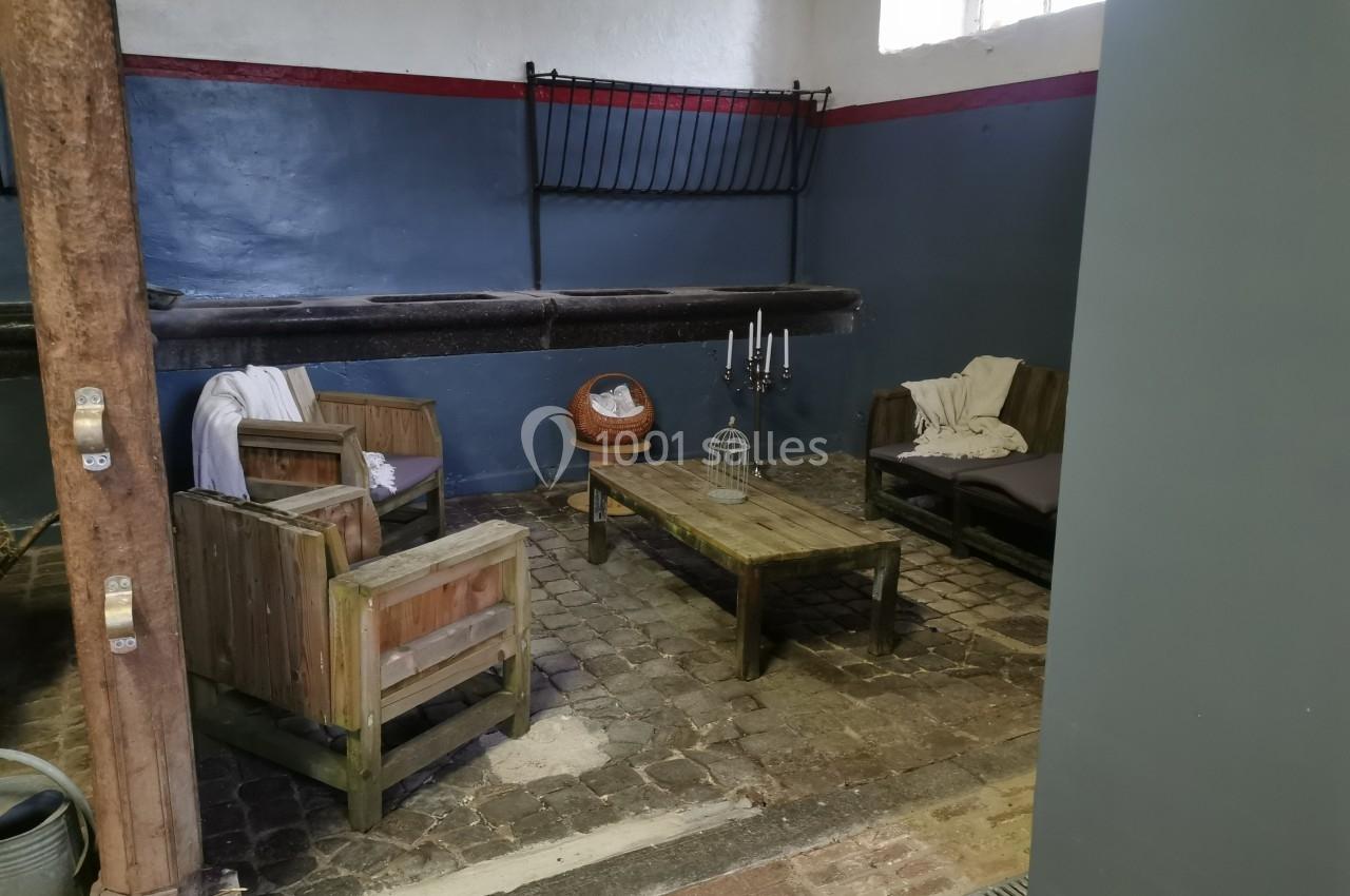 Espace intérieur rustique avec fauteuils en bois, table basse, bougeoir et panier sur un sol en pavés.