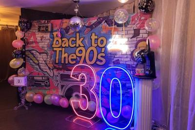 Figurines de mariés sur un gâteau décoré de fleurs bleues, d'une feuille argentée et d'un cœur en arrière-plan.