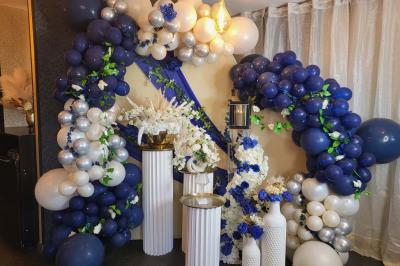 Figurines de mariés sur un gâteau décoré de fleurs bleues, d'une feuille argentée et d'un cœur en arrière-plan.