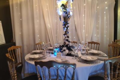 Figurines de mariés sur un gâteau décoré de fleurs bleues, d'une feuille argentée et d'un cœur en arrière-plan.