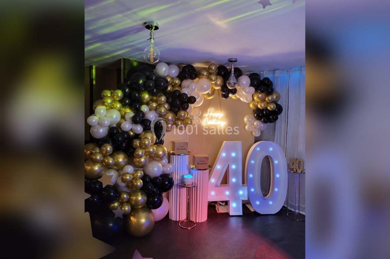 Décoration festive avec ballons noirs, blancs et dorés, chiffres lumineux ’40’ et enseigne ’Happy Birthday’.