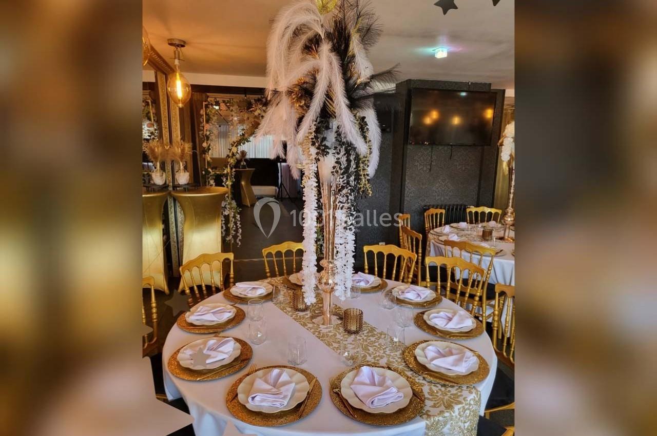 Table ronde élégamment dressée avec des assiettes dorées, serviettes pliées et un centre de table décoratif en plumes.
