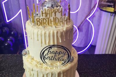 Figurines de mariés sur un gâteau décoré de fleurs bleues, d'une feuille argentée et d'un cœur en arrière-plan.