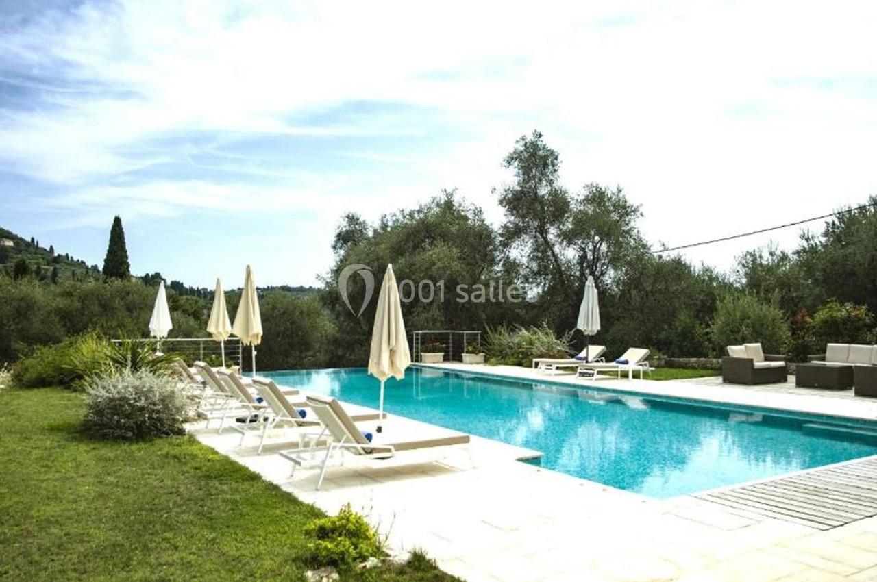 Piscine extérieure entourée de transats, parasols et végétation, avec vue sur des collines verdoyantes.