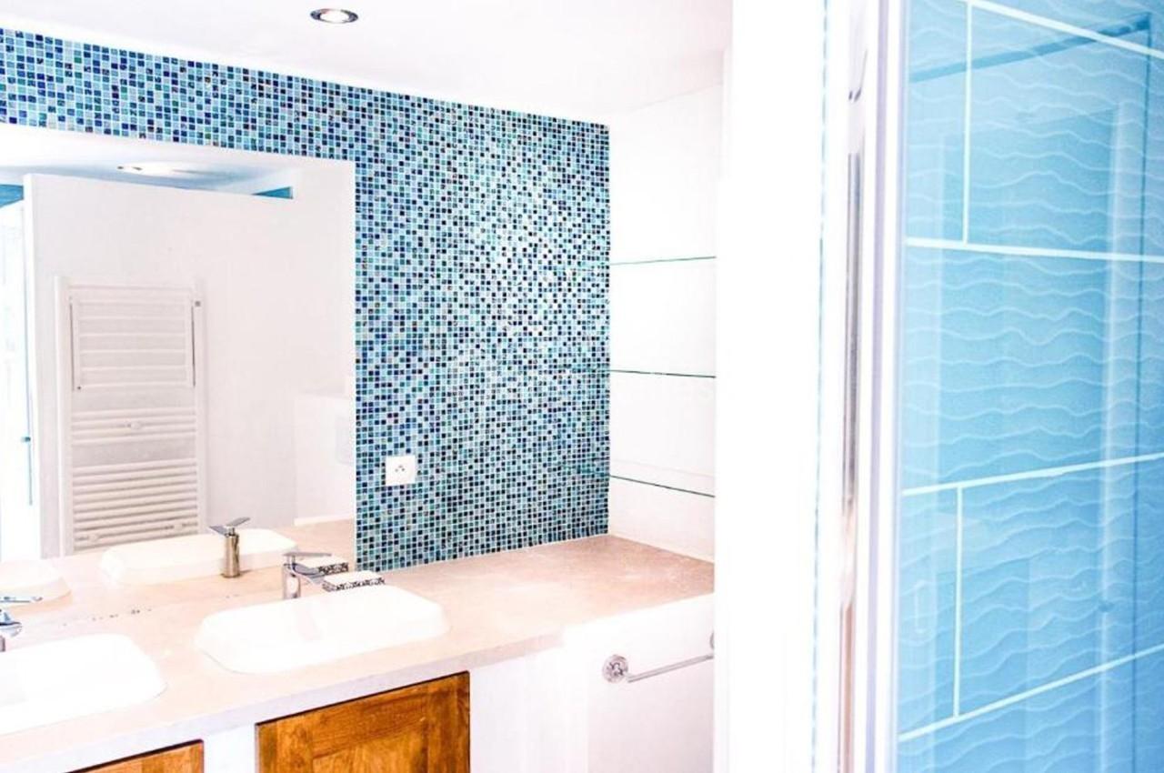 Salle de bain avec double vasque, miroir mural, carrelage mosaïque bleu et douche à paroi vitrée.