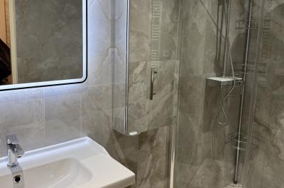 Salle de bain moderne avec lavabo, miroir éclairé, meuble de rangement et douche à paroi vitrée.