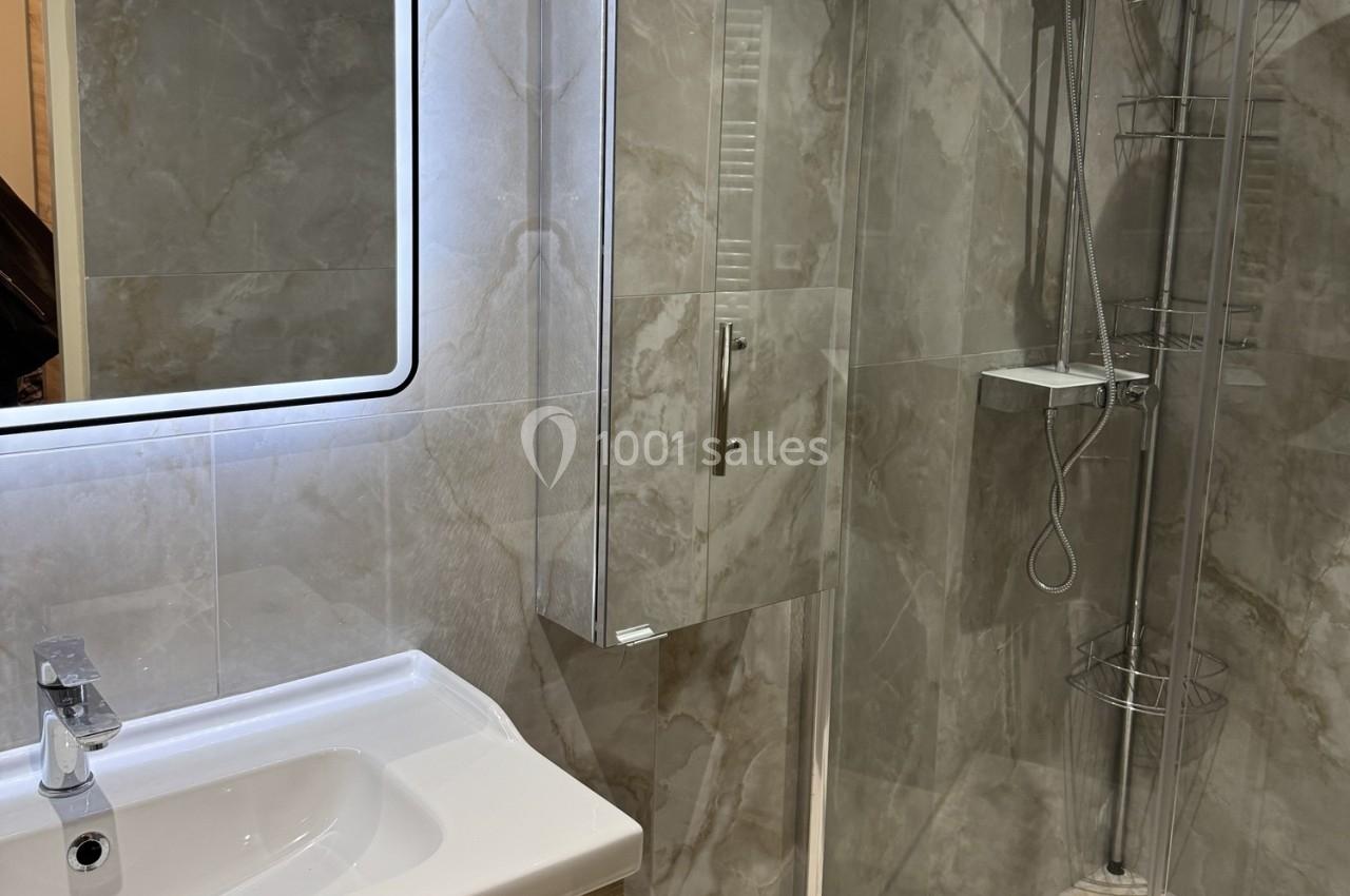 Salle de bain moderne avec lavabo, miroir éclairé, meuble de rangement et douche à paroi vitrée.