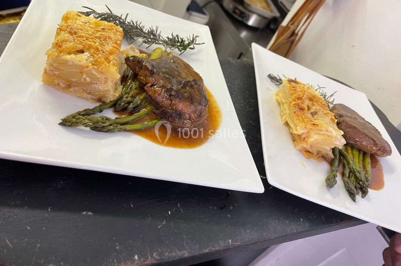 Assiette avec viande en sauce, asperges vertes et gratin dauphinois, présentée sur une table noire.