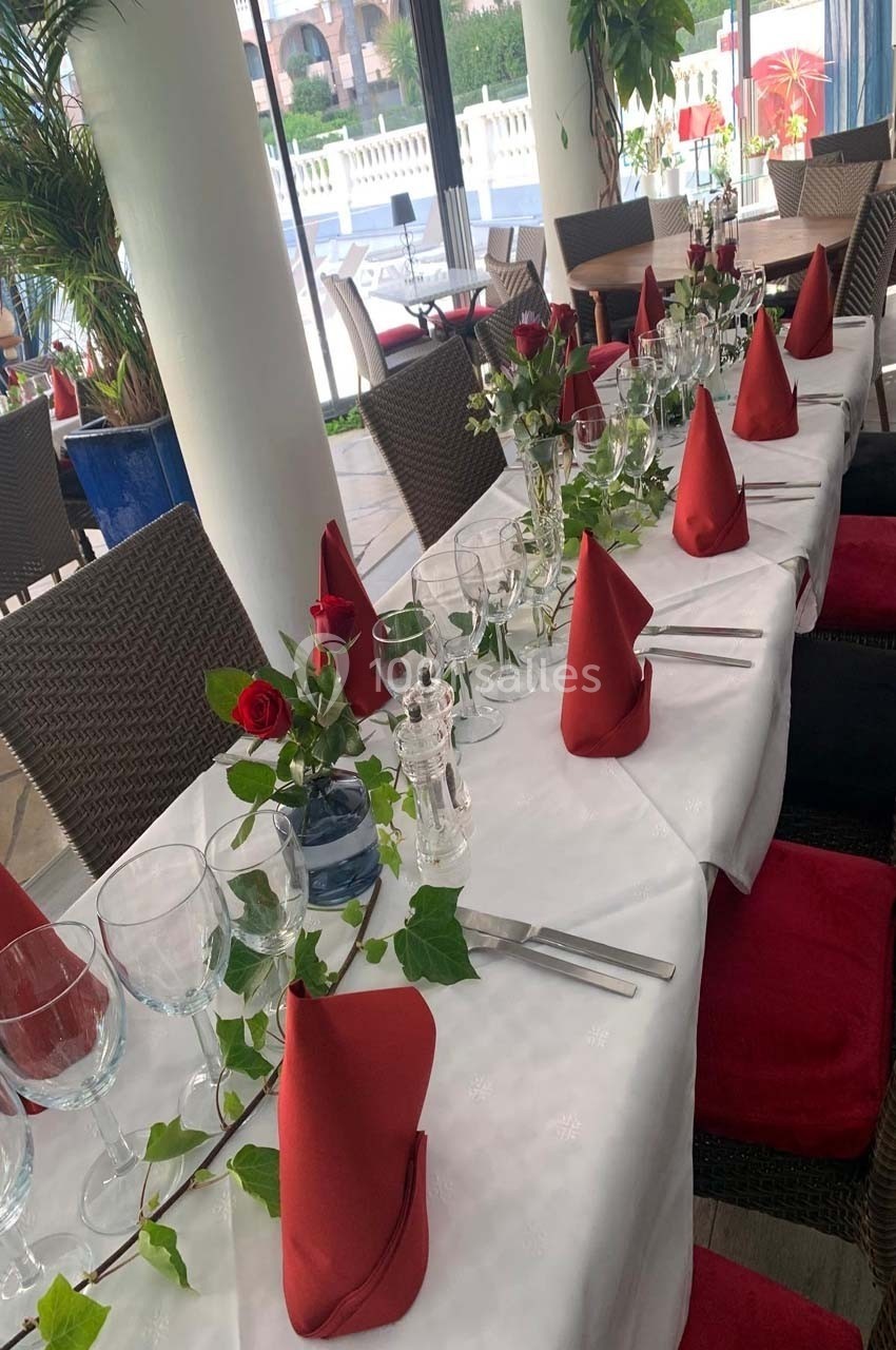 Table dressée avec nappes blanches, serviettes rouges pliées, verres, couverts et décoration florale dans un restaurant…