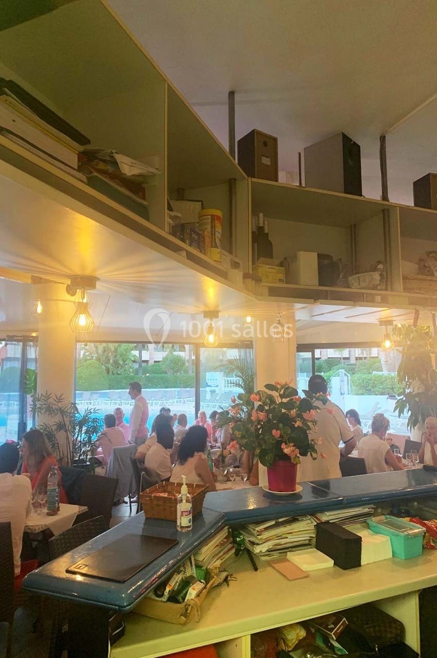 Salle de restaurant lumineuse avec des clients attablés, plantes décoratives et étagères en arrière-plan.