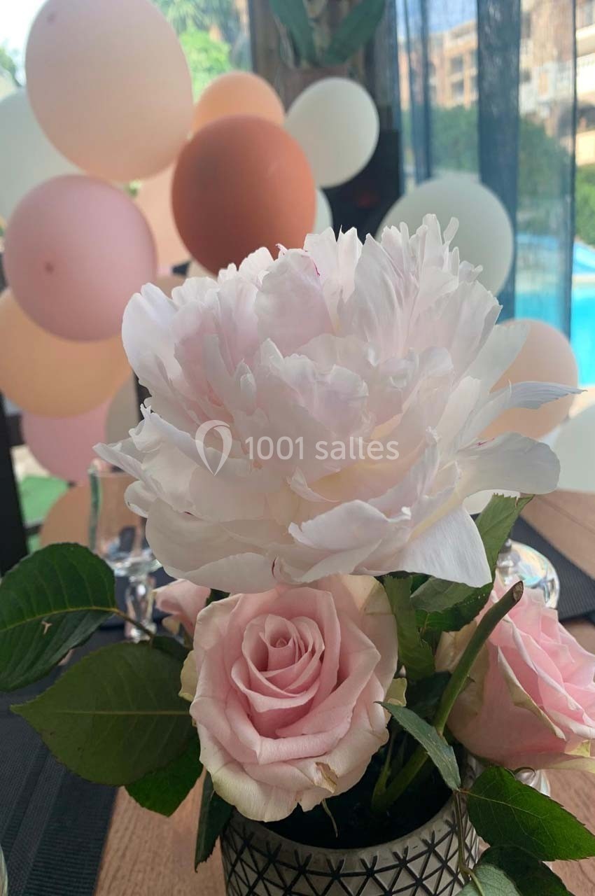 Fleurs roses et blanches dans un vase, avec des ballons flous en arrière-plan près d'une piscine.